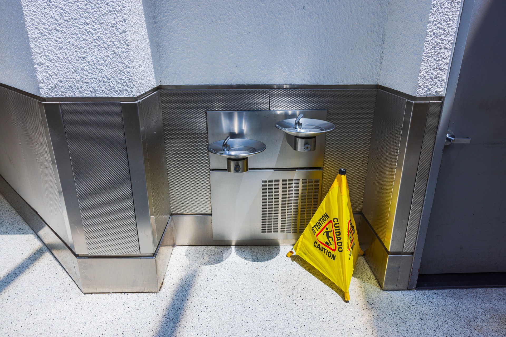 Close up view of two stainless drinking fountains with yellow caution sign standing in airport corridor. Miami. USA.